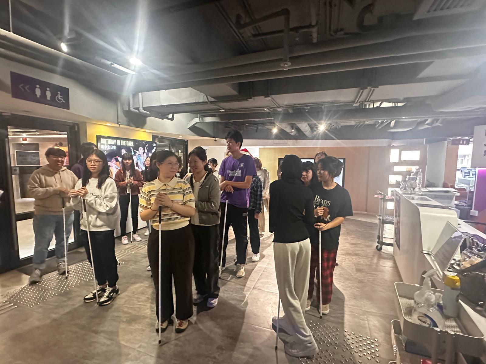 A group of individuals, holding white canes, lines up to prepare to enter the activity room.