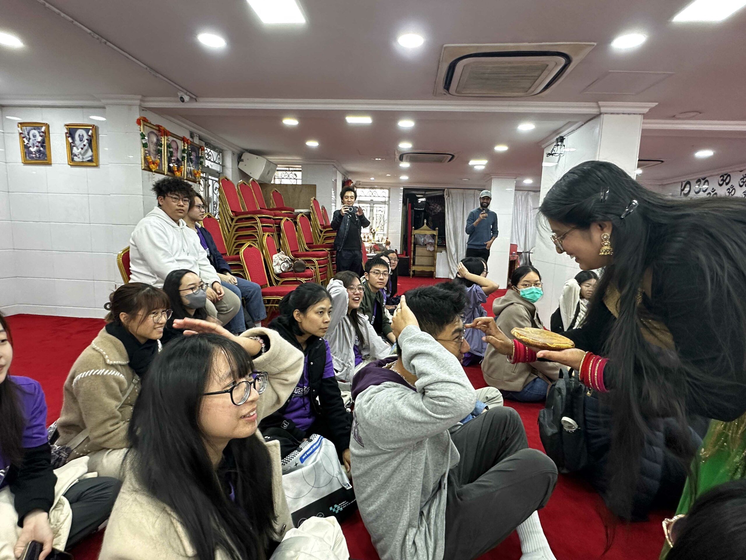 All D&I ambassadors are sitting in the Hindu temple, where an instructor is placing a Bindi on an ambassador’s forehead.