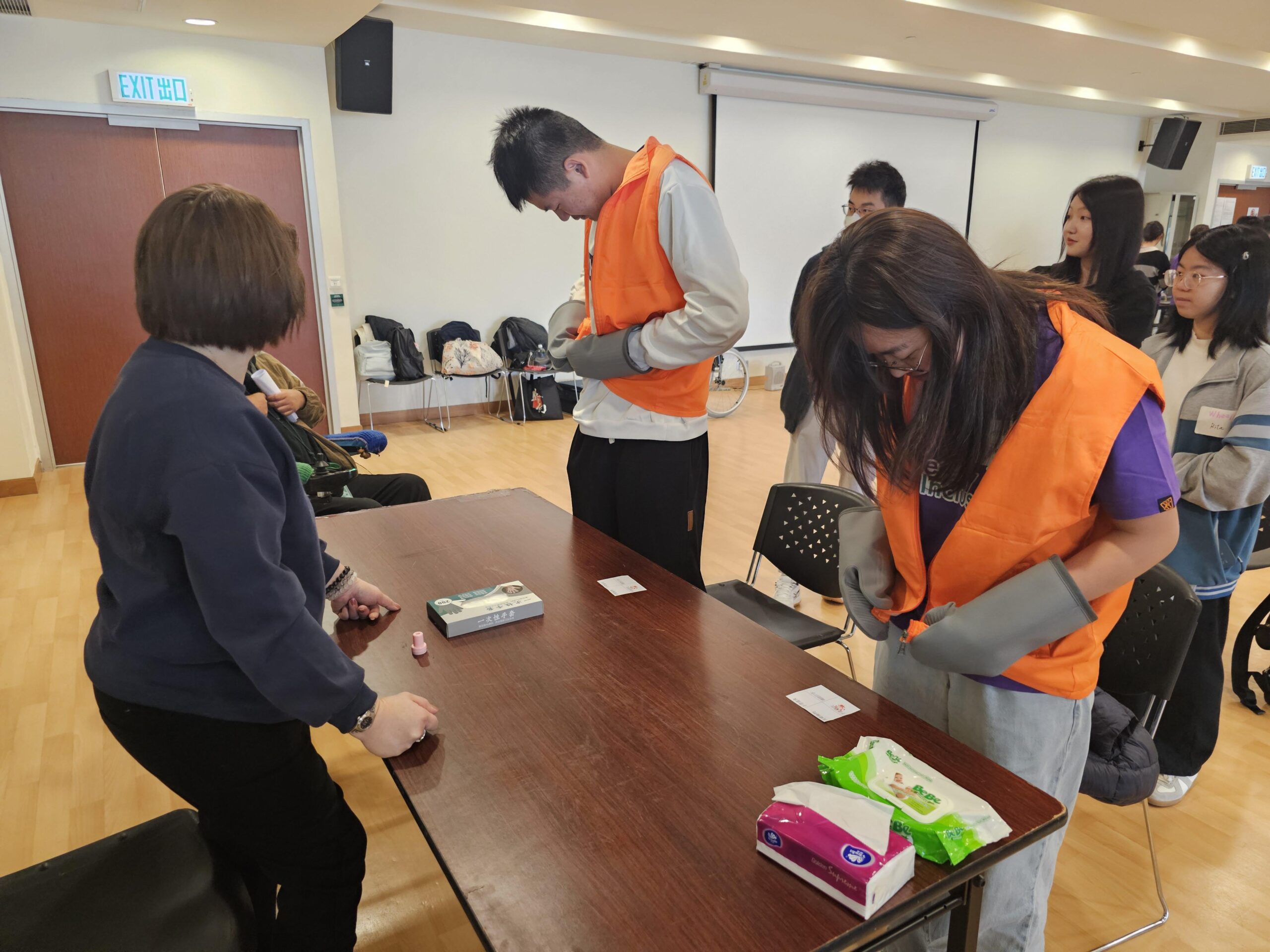 Two D&I ambassadors are wearing special vests and gloves, simulating the physical challenges faced by people with mobility impairments, as they navigate an obstacle workshop.